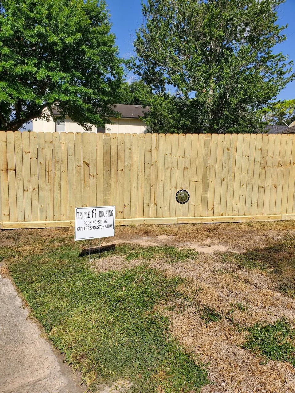 New pine privacy fence with a Triple G Roofing yard sign
