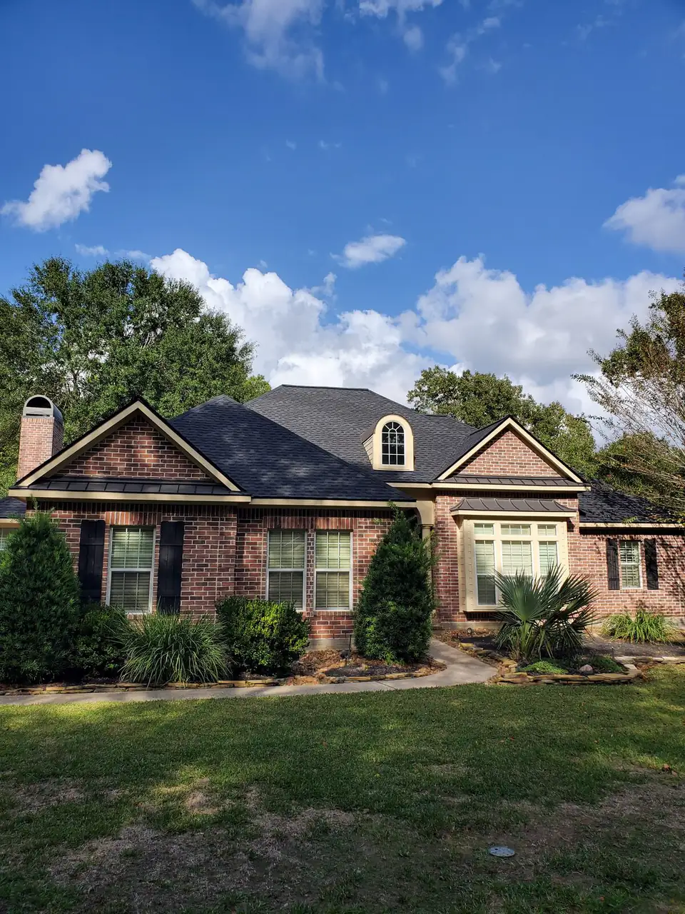 Brick home with a new dark shingle roof under mature trees