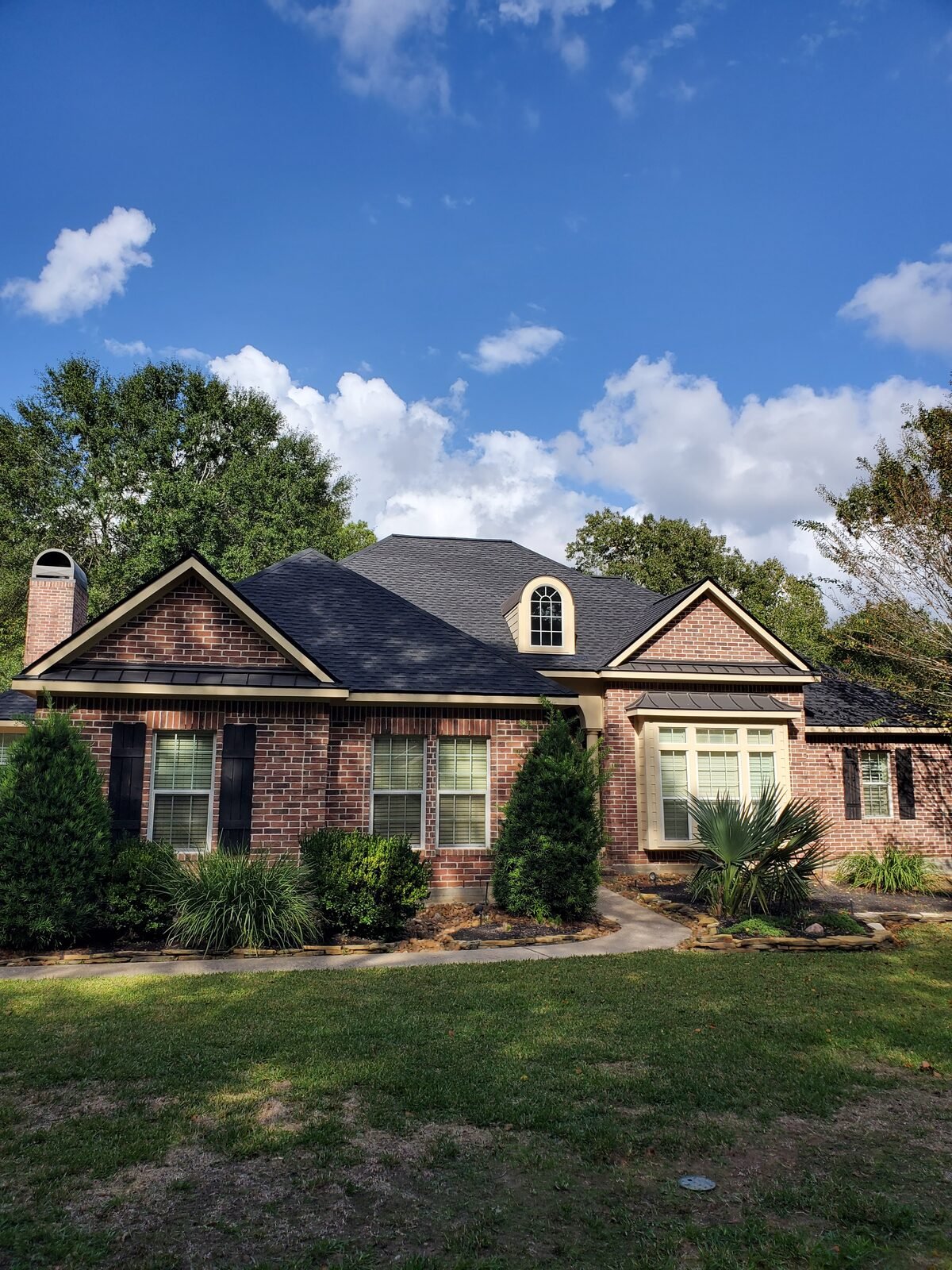Brick home with a new dark shingle roof under mature trees
