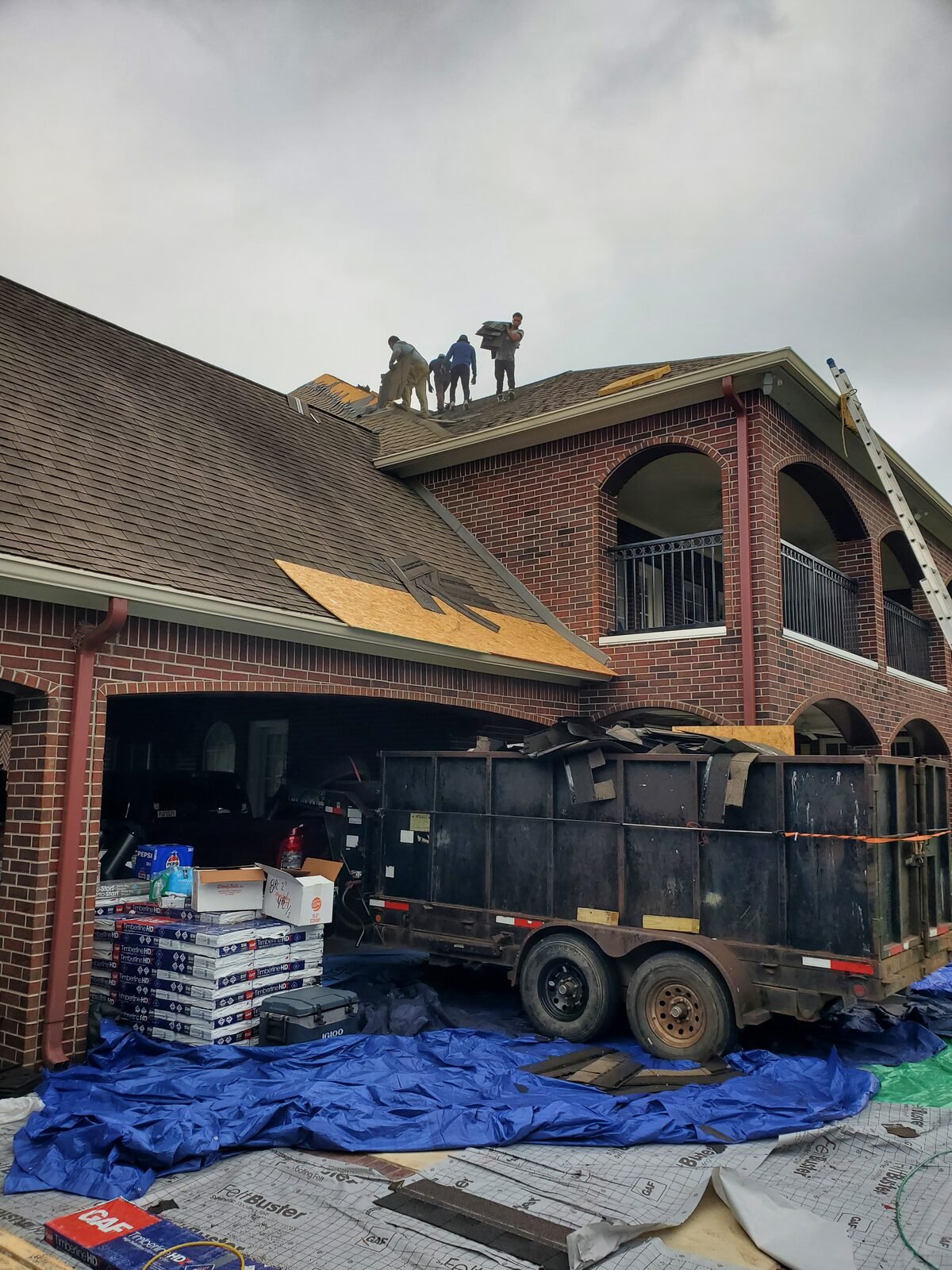 Roof tear-off in progress with a dump trailer staged in the driveway