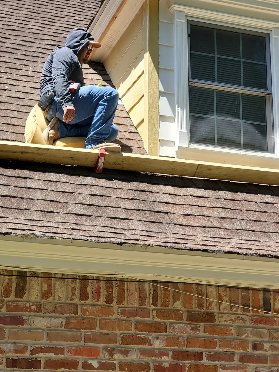 Crew member replacing siding on a dormer above a shingle roof