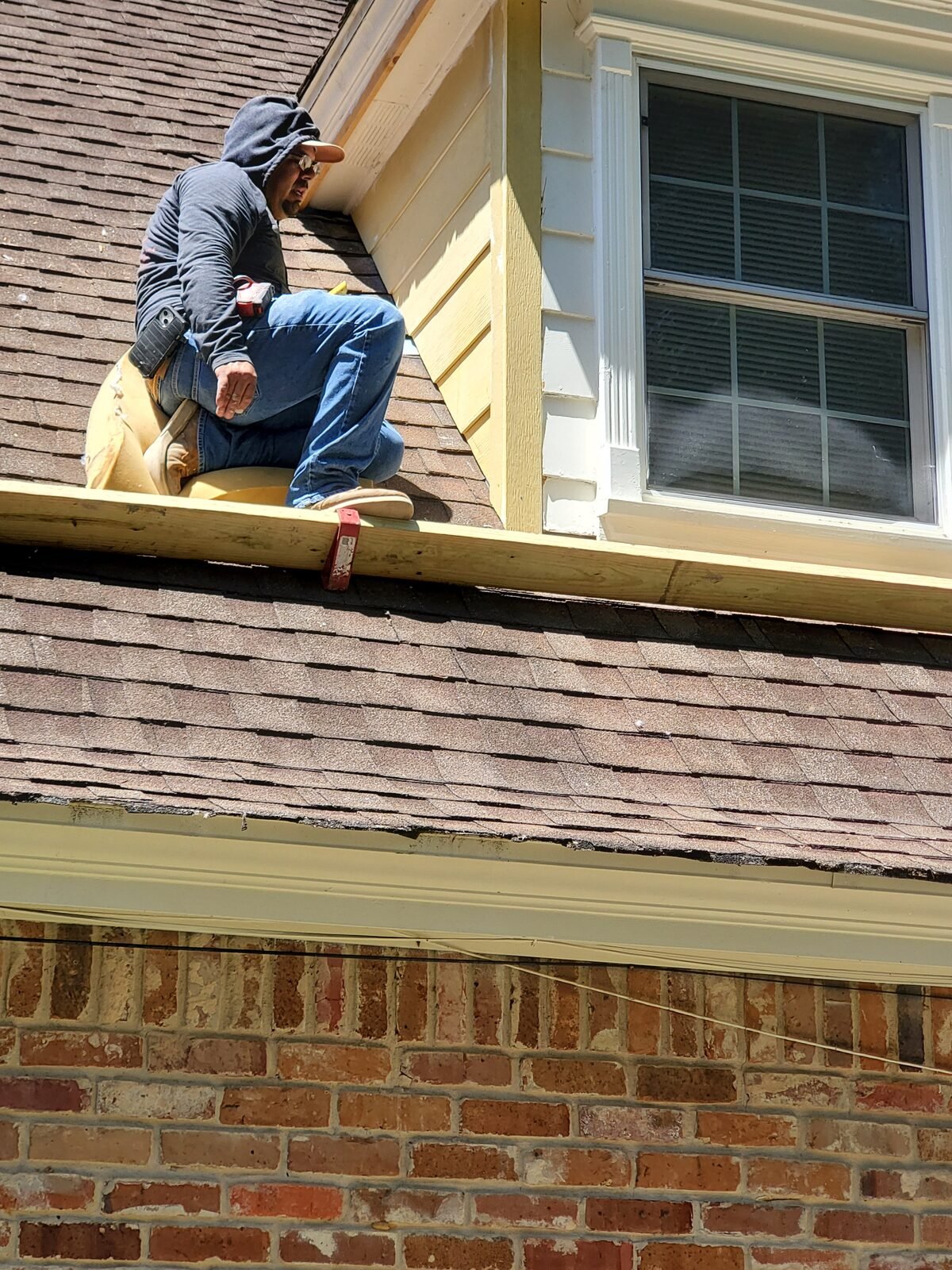 Crew member replacing siding on a dormer above a shingle roof